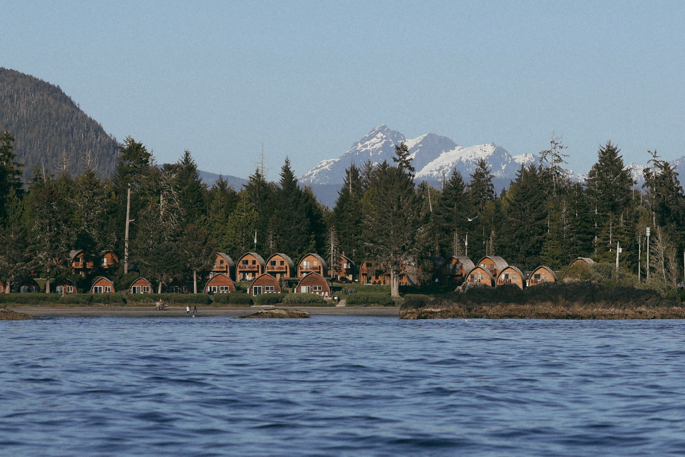 Beehive shaped cabins on the edge of the sea with snow capped mountains in background