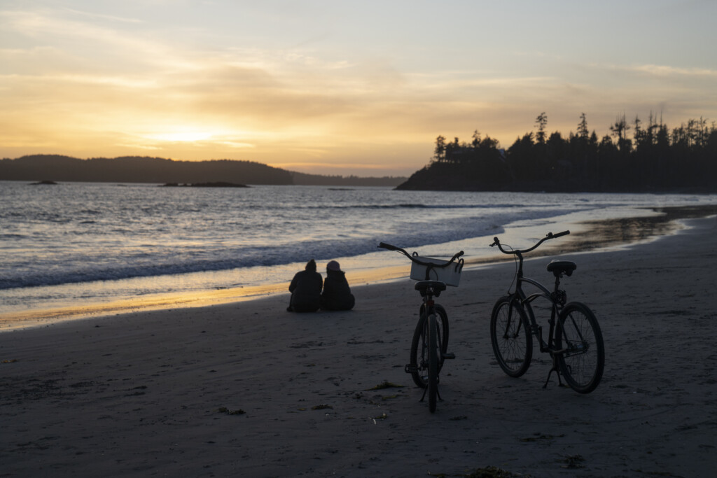 Couple watches sunset from the beach with their bikes parked in the foreground