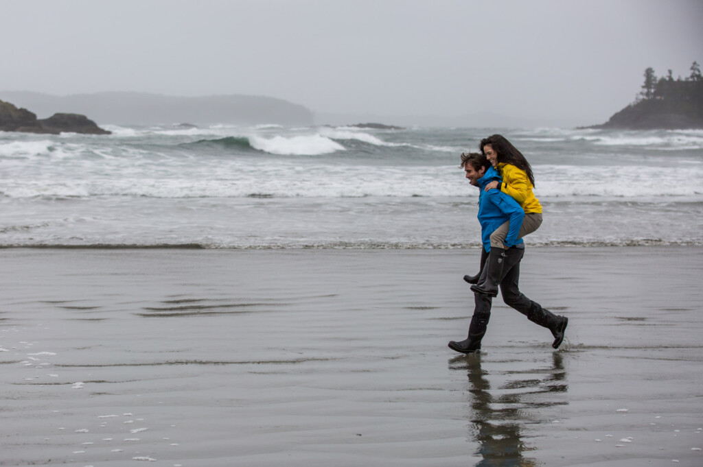 Man giving women piggyback on the beach in tofino with waves in background